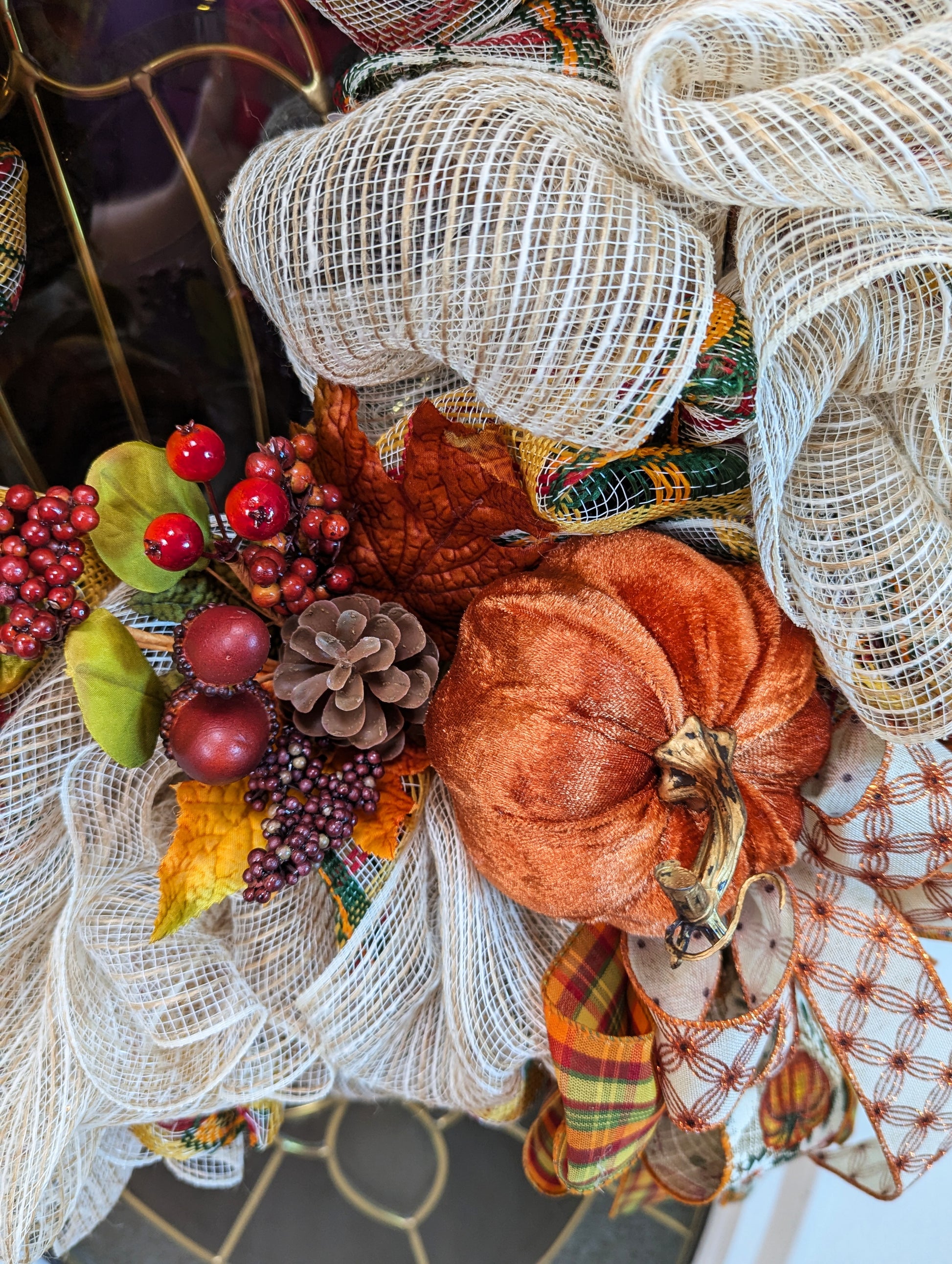 Fall Wreath with beige deco mesh base with a curly Q design. There are 2 matching bows with orange, gold, green and beige patterned ribbons. It has a velveteen pumpkin, acorns, pinecones and fall foliage.