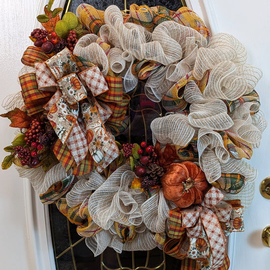 Fall Wreath with beige deco mesh base with a curly Q design. There are 2 matching bows with orange, gold, green and beige patterned ribbons. It has a velveteen pumpkin, acorns, pinecones and fall foliage.